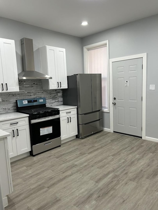 kitchen featuring white cabinets, wall chimney exhaust hood, appliances with stainless steel finishes, tasteful backsplash, and light hardwood / wood-style floors