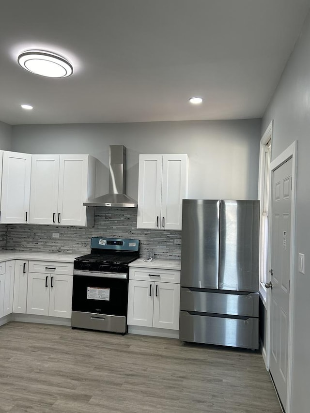 kitchen featuring wall chimney exhaust hood, stainless steel appliances, tasteful backsplash, light hardwood / wood-style flooring, and white cabinets