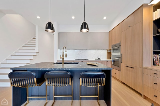 kitchen featuring light brown cabinetry, decorative light fixtures, a center island with sink, and sink