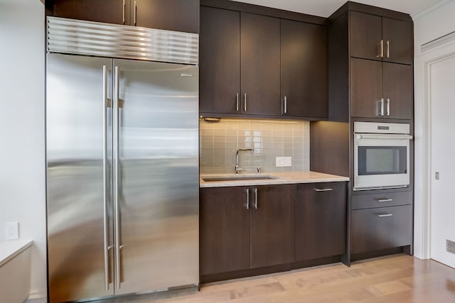 kitchen with dark brown cabinetry, sink, stainless steel appliances, and light wood-type flooring