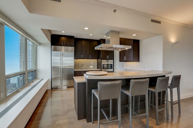 kitchen featuring a breakfast bar, ventilation hood, stainless steel appliances, and dark brown cabinets