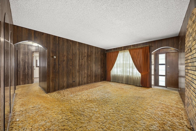 empty room featuring carpet flooring, a textured ceiling, and wood walls