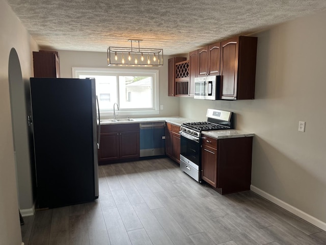 kitchen featuring appliances with stainless steel finishes, decorative light fixtures, sink, dark brown cabinets, and light wood-type flooring