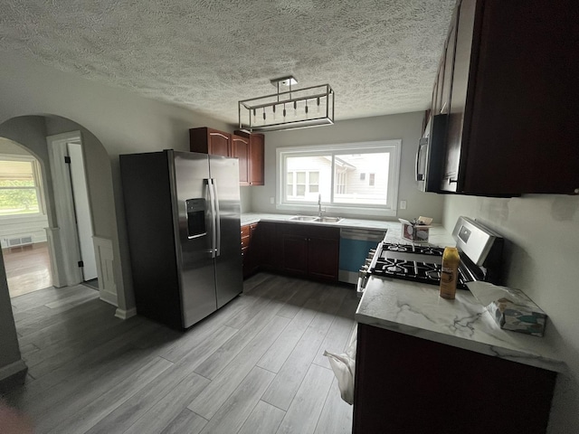 kitchen with sink, light stone counters, light hardwood / wood-style floors, stainless steel appliances, and a textured ceiling