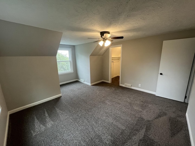 bonus room featuring ceiling fan, vaulted ceiling, a textured ceiling, and dark colored carpet