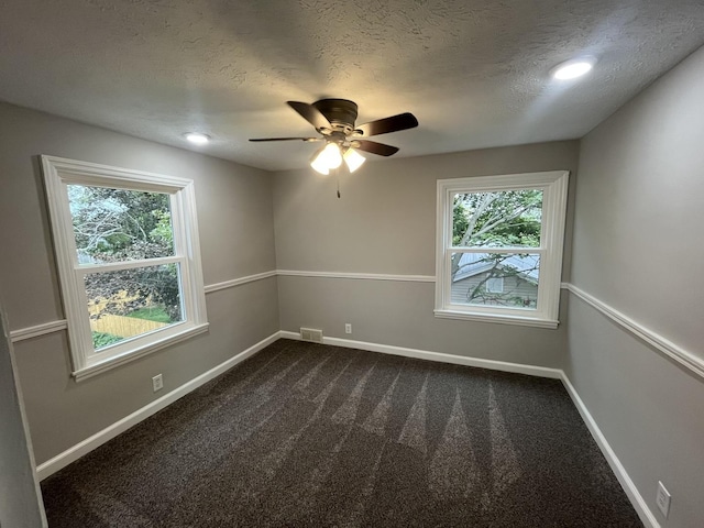 empty room featuring ceiling fan, dark carpet, and a textured ceiling