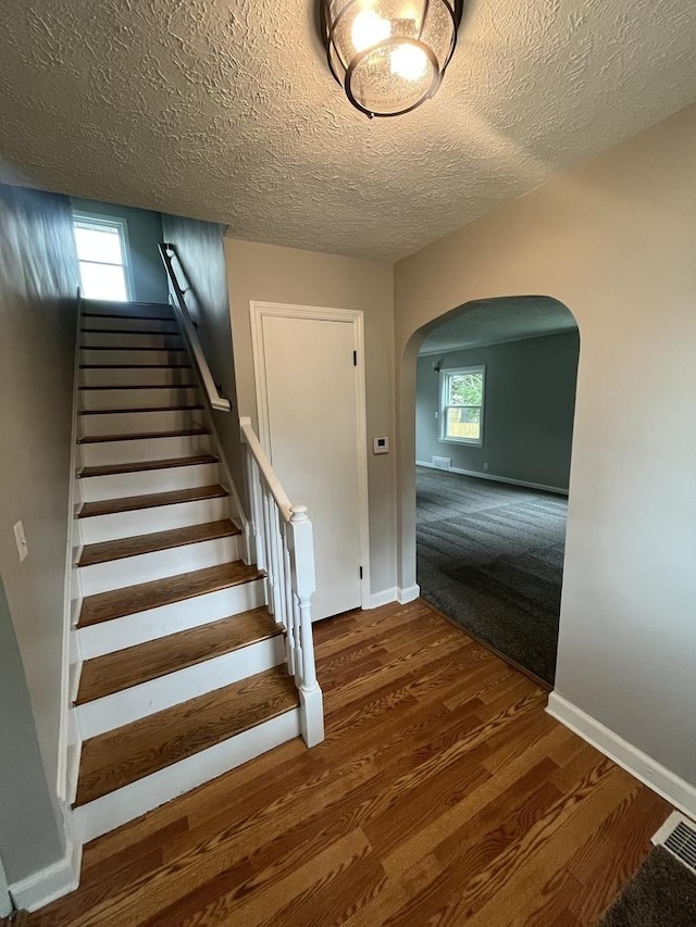 stairs with a healthy amount of sunlight, wood-type flooring, and a textured ceiling