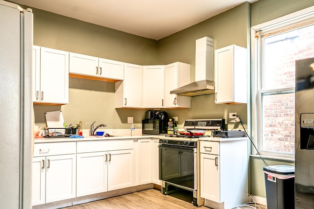 kitchen featuring white cabinets, wall chimney exhaust hood, plenty of natural light, and range