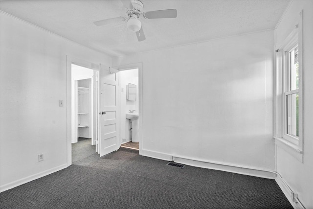 unfurnished bedroom featuring a walk in closet, dark carpet, a textured ceiling, ceiling fan, and connected bathroom