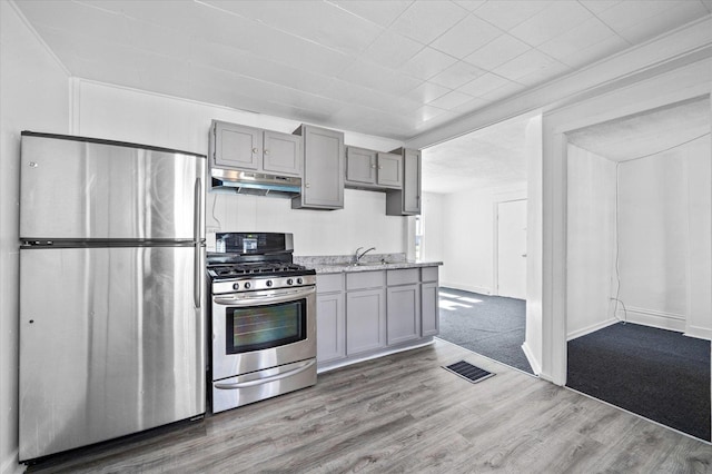 kitchen with light stone countertops, stainless steel appliances, sink, hardwood / wood-style flooring, and gray cabinets