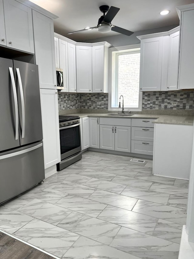 kitchen featuring ceiling fan, sink, decorative backsplash, white cabinets, and appliances with stainless steel finishes