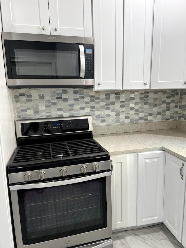 kitchen with backsplash, stainless steel appliances, light stone counters, and white cabinetry