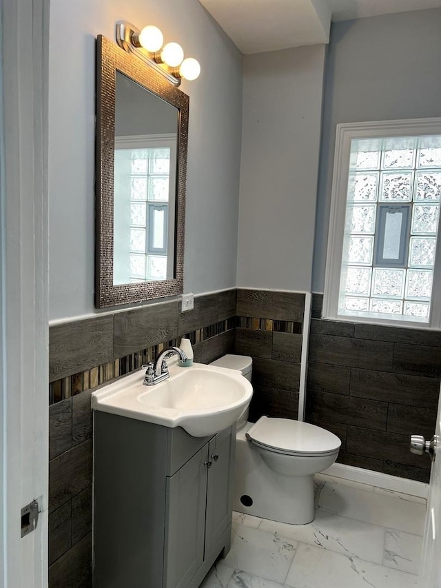 bathroom with a wealth of natural light, vanity, tile walls, and toilet