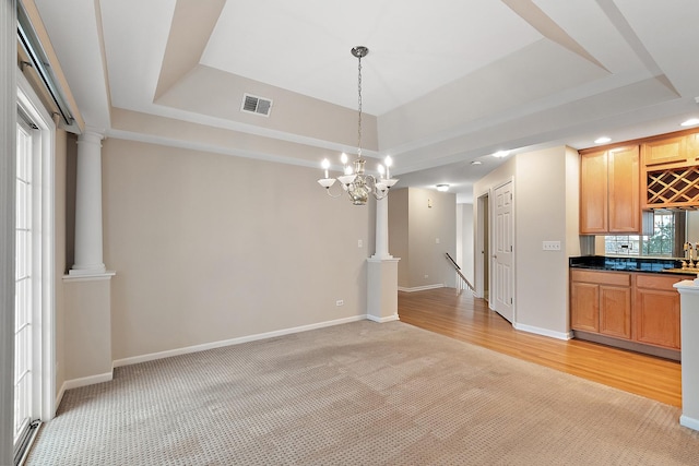 unfurnished dining area with decorative columns, light colored carpet, a tray ceiling, and an inviting chandelier