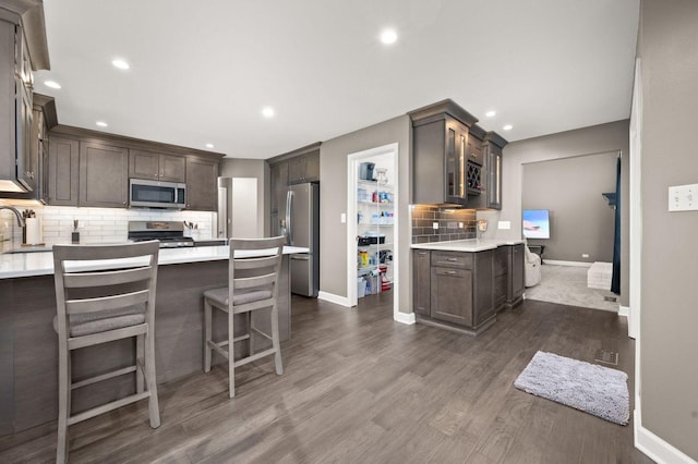 kitchen with appliances with stainless steel finishes, sink, backsplash, dark brown cabinetry, and dark wood-type flooring