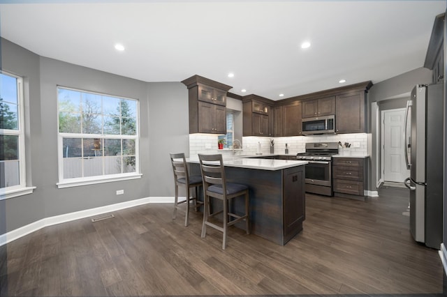 kitchen featuring a kitchen island, appliances with stainless steel finishes, dark hardwood / wood-style floors, backsplash, and dark brown cabinetry