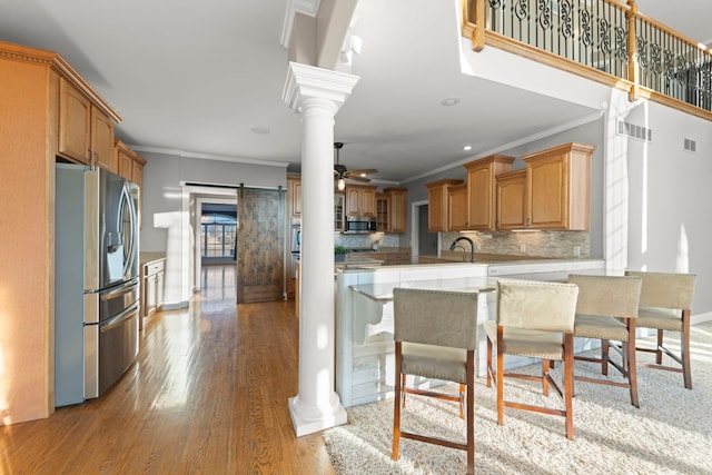 kitchen with ceiling fan, decorative backsplash, crown molding, appliances with stainless steel finishes, and ornate columns