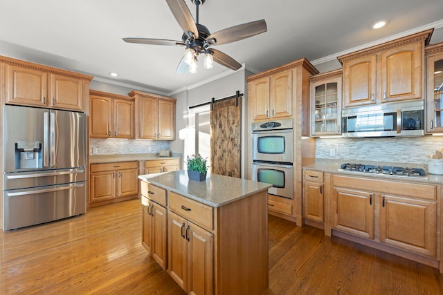 kitchen with a barn door, decorative backsplash, crown molding, stainless steel appliances, and light stone counters