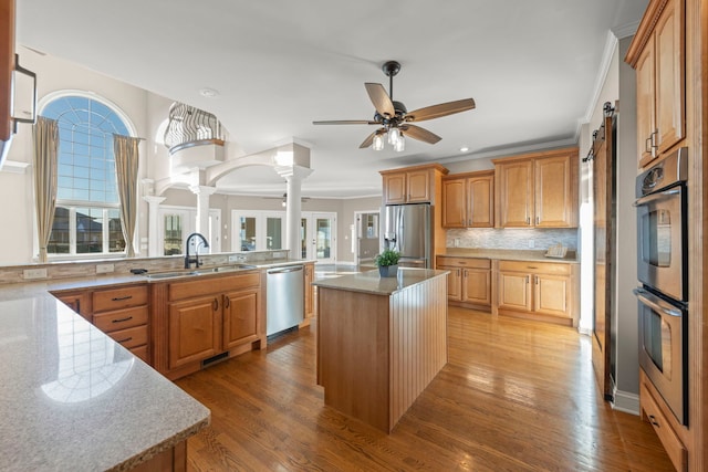 kitchen featuring tasteful backsplash, a kitchen island, sink, stainless steel appliances, and decorative columns