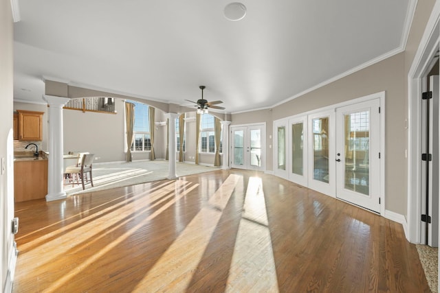 unfurnished living room featuring wood-type flooring, ornate columns, french doors, ornamental molding, and ceiling fan