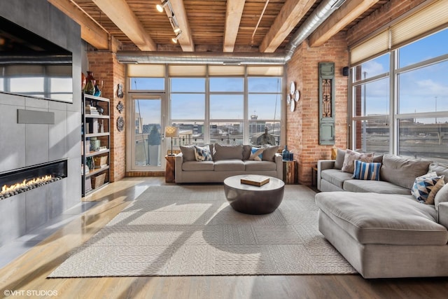 living room with a large fireplace, wood ceiling, track lighting, hardwood / wood-style flooring, and beam ceiling