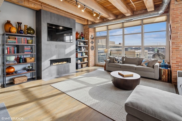 living room featuring wood ceiling, rail lighting, a fireplace, wood-type flooring, and beamed ceiling