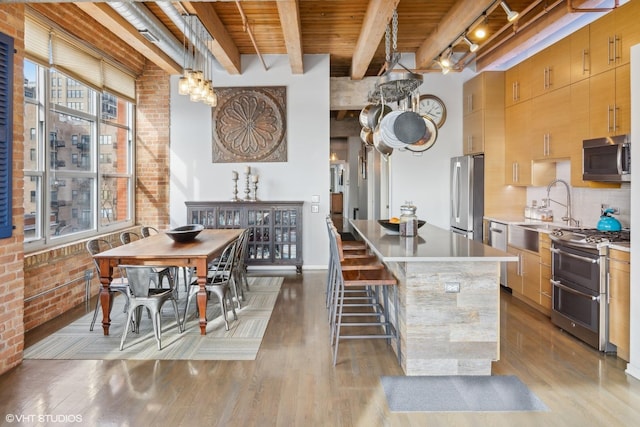 kitchen featuring decorative light fixtures, brick wall, beam ceiling, appliances with stainless steel finishes, and wooden ceiling