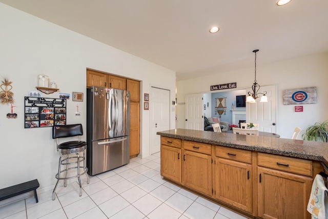 kitchen featuring decorative light fixtures, dark stone countertops, stainless steel refrigerator, and light tile patterned floors