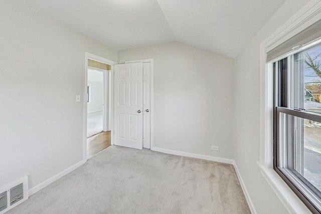 spare room with light carpet, a wealth of natural light, and vaulted ceiling