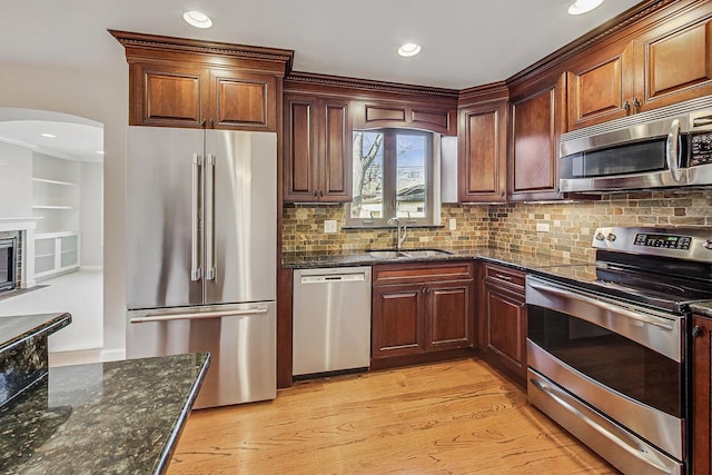 kitchen featuring sink, tasteful backsplash, dark stone counters, appliances with stainless steel finishes, and light wood-type flooring