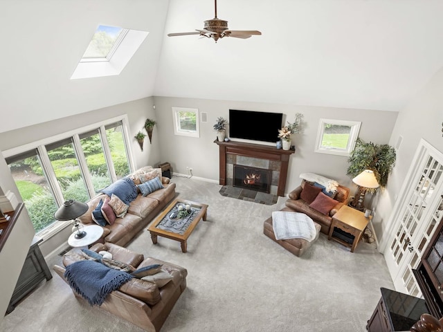 carpeted living room featuring a skylight, high vaulted ceiling, ceiling fan, and a premium fireplace