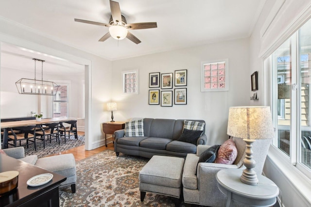 living area featuring ceiling fan with notable chandelier, baseboards, wood finished floors, and a healthy amount of sunlight