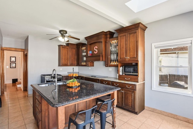 kitchen with dark stone counters, a sink, a skylight, ceiling fan, and stainless steel microwave