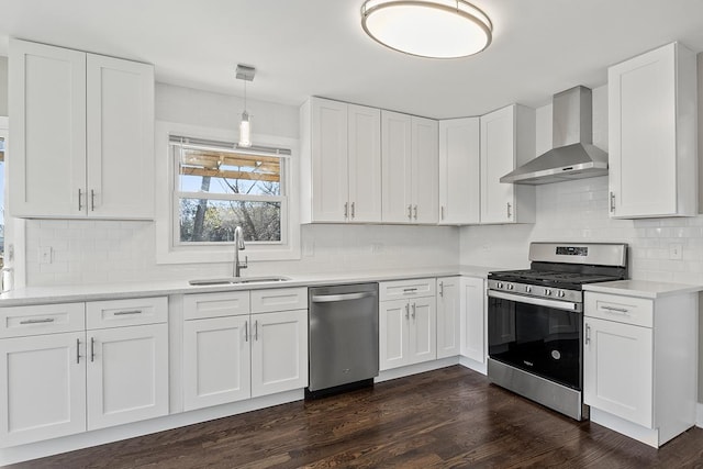 kitchen with sink, appliances with stainless steel finishes, white cabinetry, decorative light fixtures, and wall chimney exhaust hood