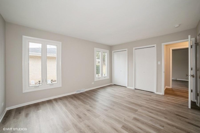 unfurnished bedroom with light hardwood / wood-style flooring, multiple windows, and multiple closets