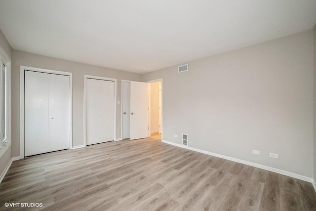 unfurnished bedroom with two closets and light wood-type flooring