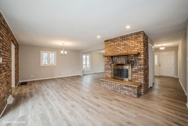 unfurnished living room with light wood-type flooring, an inviting chandelier, and a brick fireplace