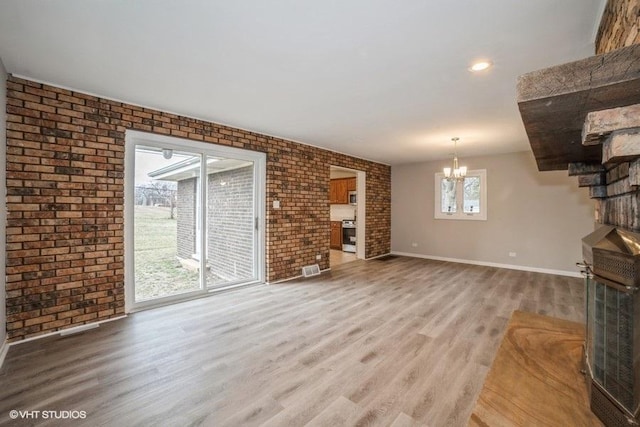 unfurnished living room with a chandelier, brick wall, and light wood-type flooring