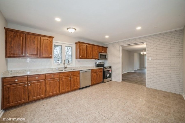 kitchen featuring light stone counters, brick wall, stainless steel appliances, sink, and a notable chandelier