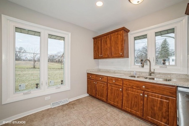 kitchen with light tile patterned floors, light stone counters, stainless steel dishwasher, and sink