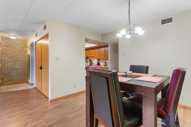 dining room with light hardwood / wood-style flooring, a chandelier, and brick wall