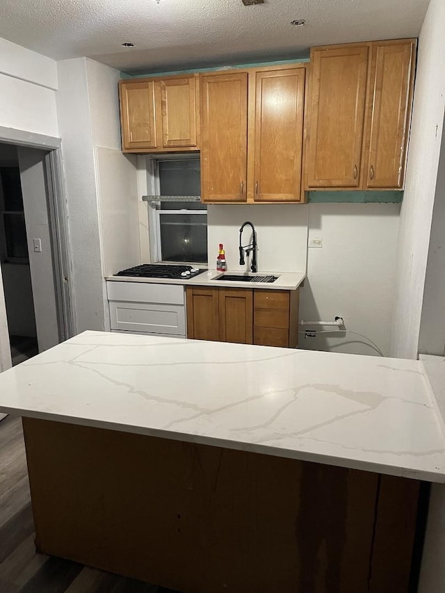 kitchen with a textured ceiling, dark wood-type flooring, stainless steel gas cooktop, and sink