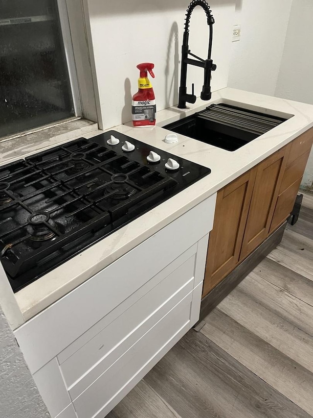 kitchen with light hardwood / wood-style floors, black gas cooktop, and sink