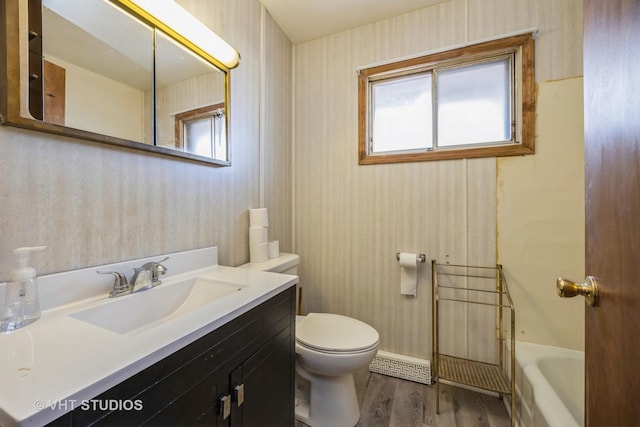 full bath with a tub to relax in, vanity, toilet, and wood finished floors