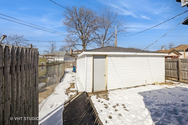 snow covered structure featuring an outdoor structure and fence