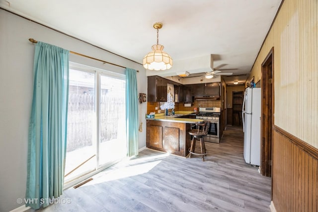 kitchen with a peninsula, wainscoting, freestanding refrigerator, a kitchen bar, and gas range