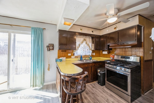 kitchen with gas stove, a sink, under cabinet range hood, and dark brown cabinetry