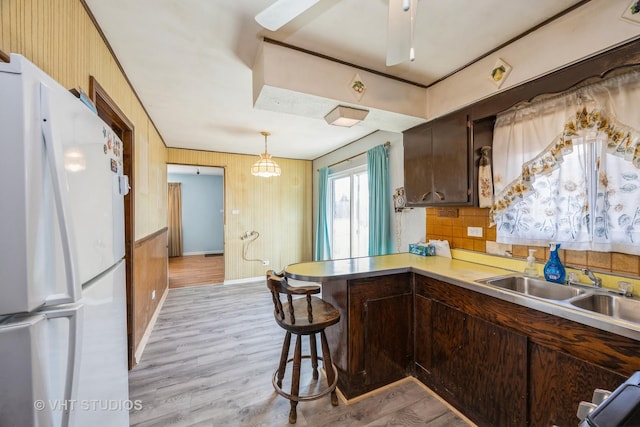 kitchen with freestanding refrigerator, light countertops, light wood-type flooring, a kitchen bar, and pendant lighting