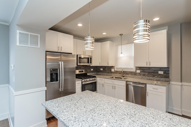 kitchen featuring appliances with stainless steel finishes, backsplash, sink, decorative light fixtures, and white cabinetry