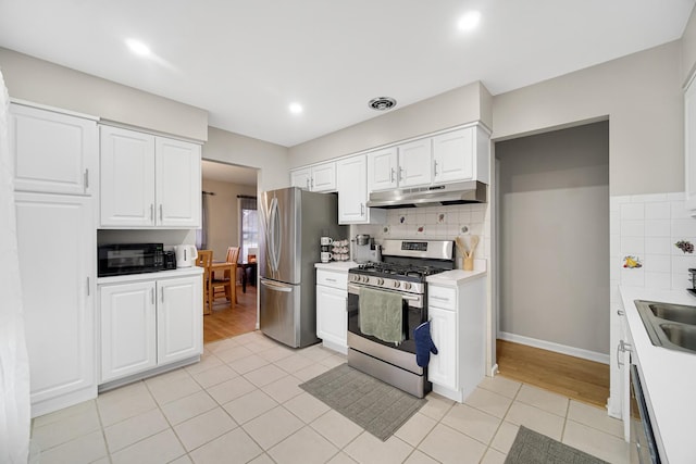 kitchen with light tile patterned floors, backsplash, stainless steel appliances, and white cabinetry